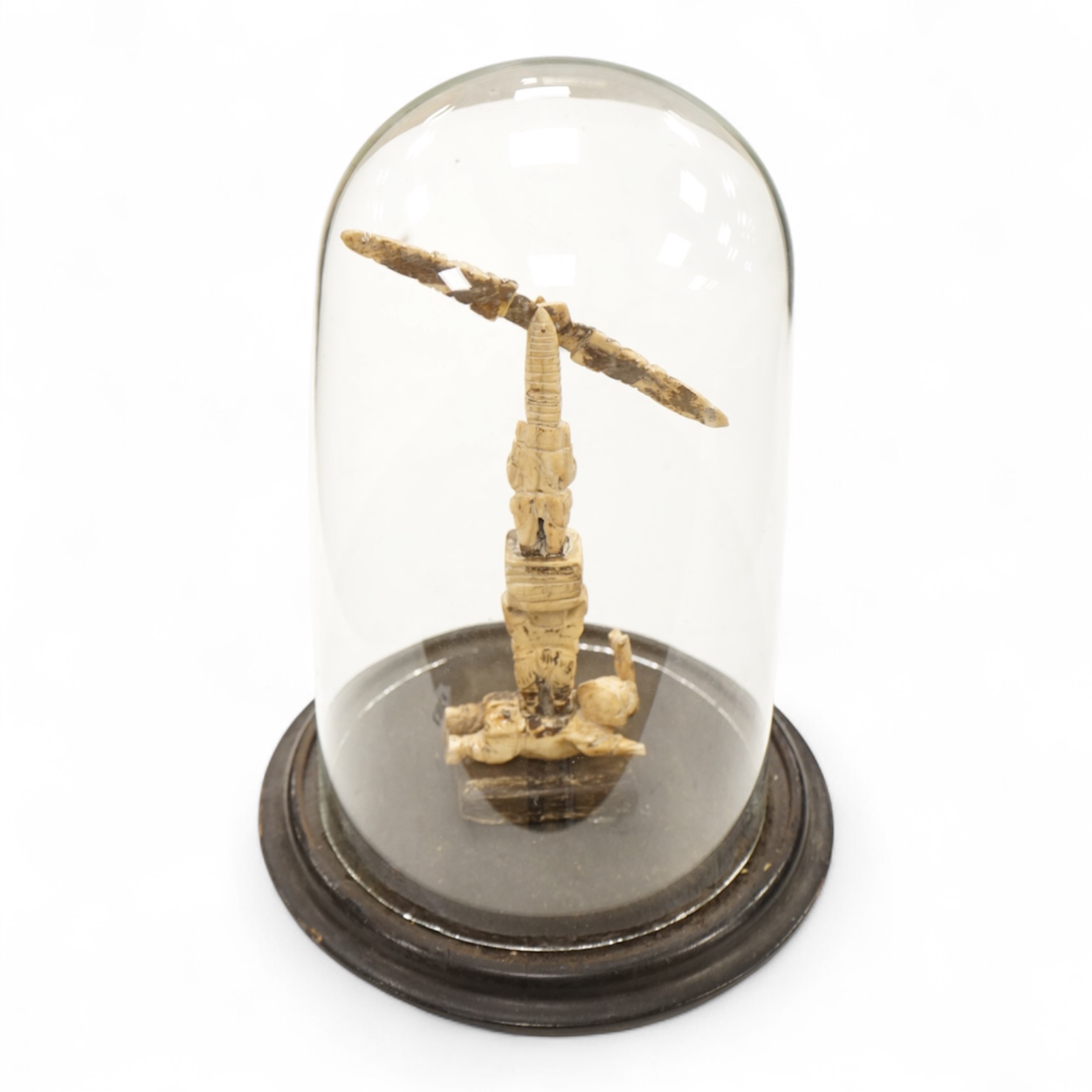 A 19th century Indian bone sculptural devotional object, carved as a totem with Ganesh and other deities, pivoting beam, 18cm high, glass dome with ebonised base